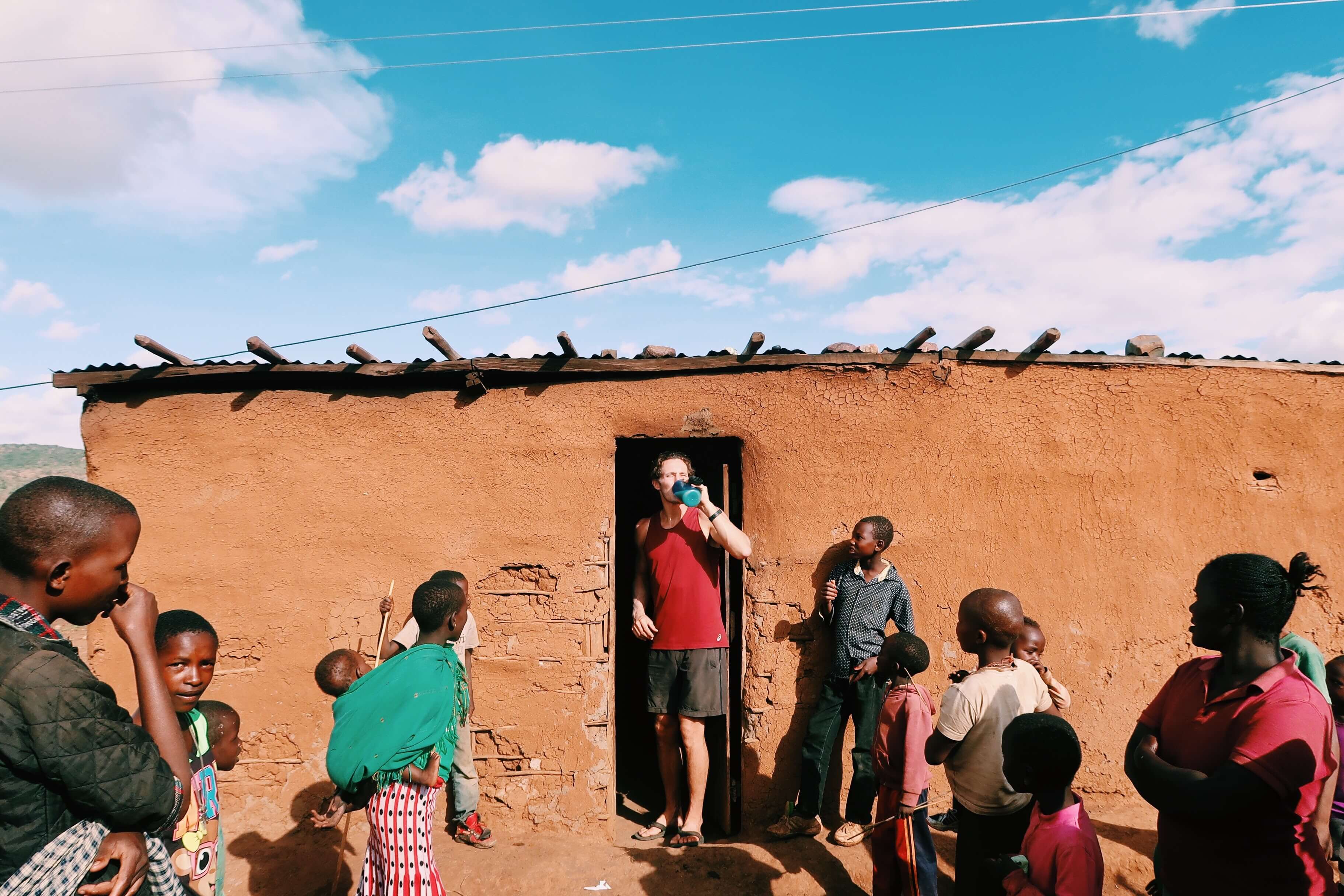 Chris emerging from a hut with Maasai wine surrounded by curious locals