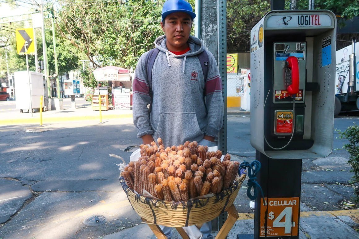 Young man selling churros from a basket on the street