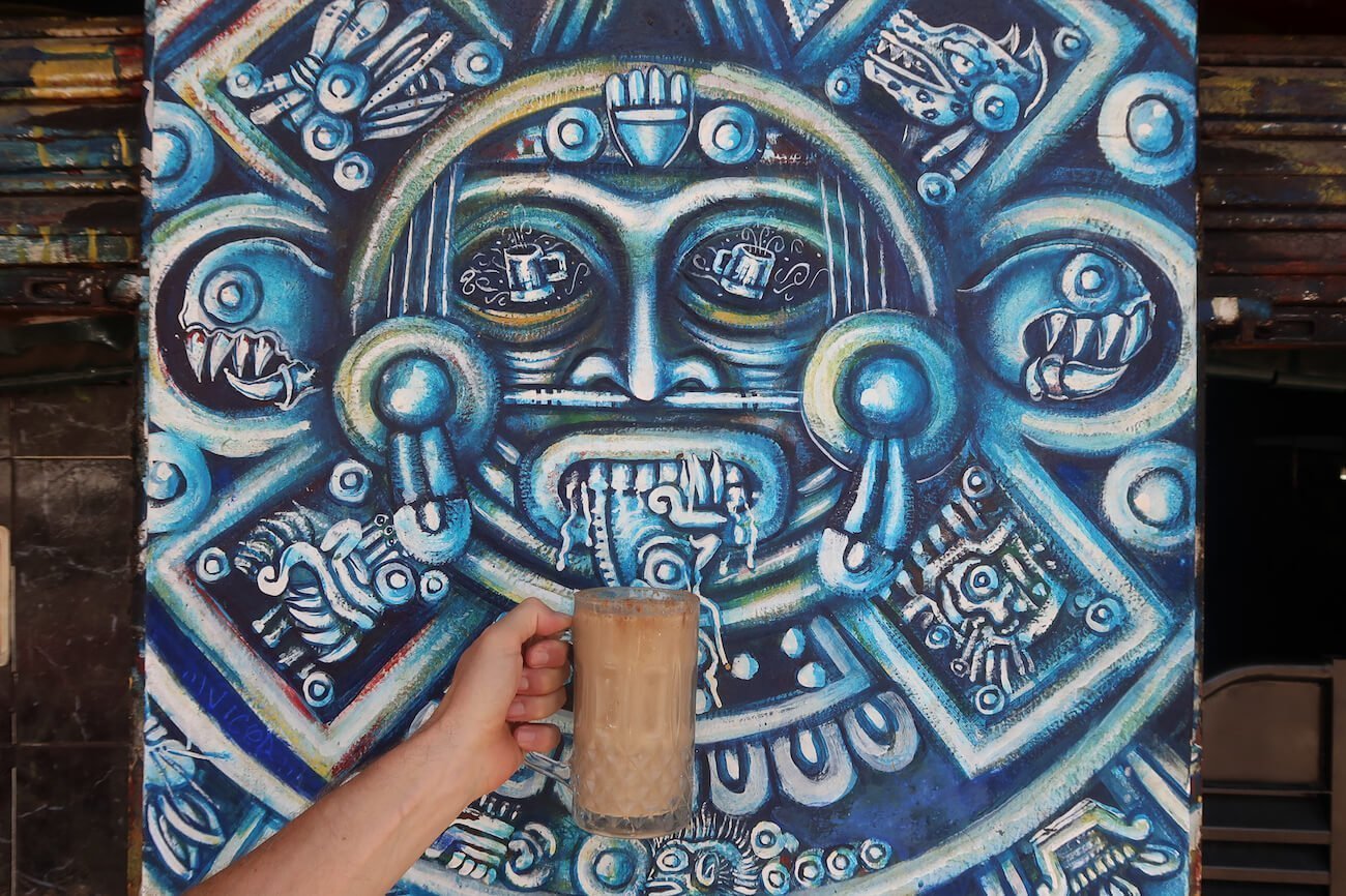 Wall painting at a Mexico City pulqueria with someone holding a mug of pulque below it