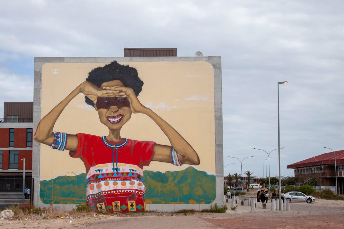 Things to do in Cape Town - visit a township like Khayletisha. Graffiti of lady shielding her eyes from the sun with Table Mountain in the background.