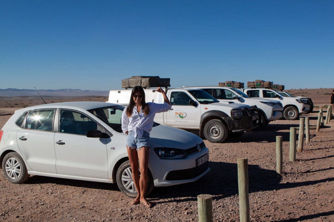 Kim showing us her guns beside the other camping 4x4s and our tiny Volkswagen Polo in a parking lot in Fish River Canyon