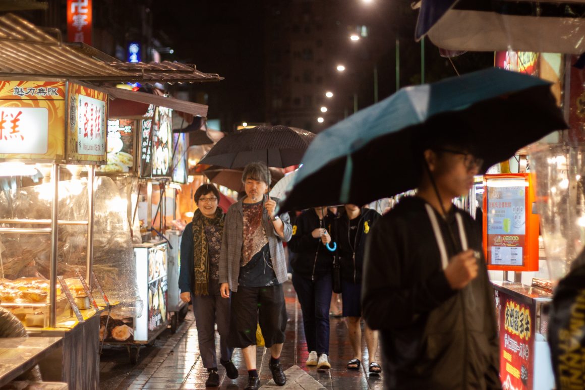 Umbrellas and local Taiwanese people walking the narrow Taipei streets at a local night market