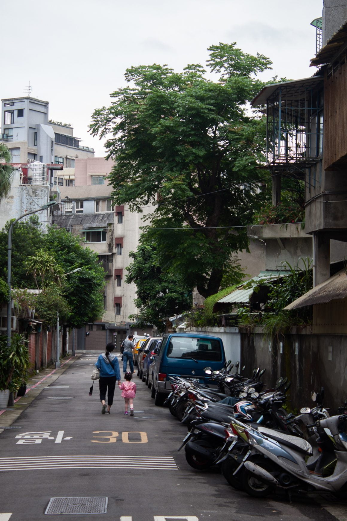 Mother and daughter hold hands walking down a quiet street in Taipei