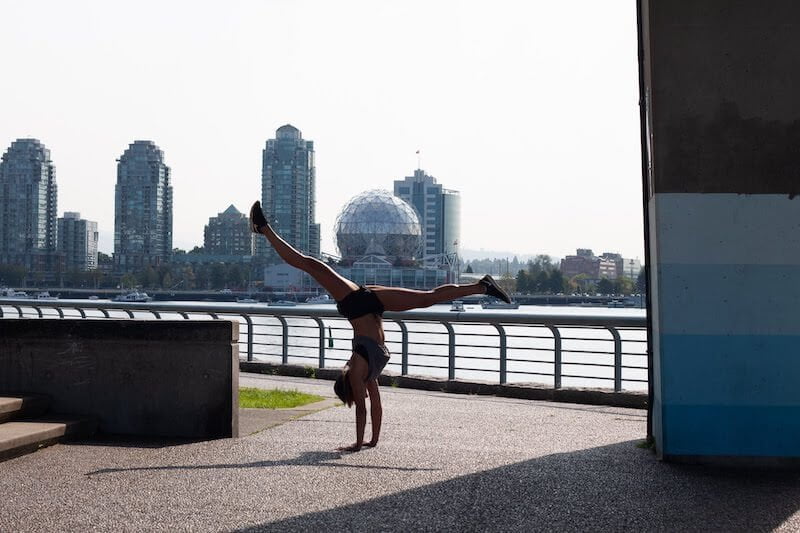 Kim doing a handstand on the Seawall under Cambie Bridge with Science World in the background.