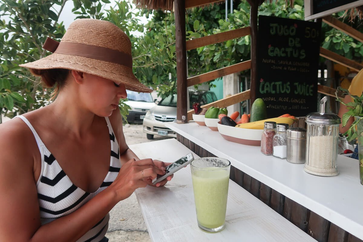 Kim checking her phone sipping a green smoothie in Tulum, Mexico.. or maybe looking for travel insurance when already traveling.