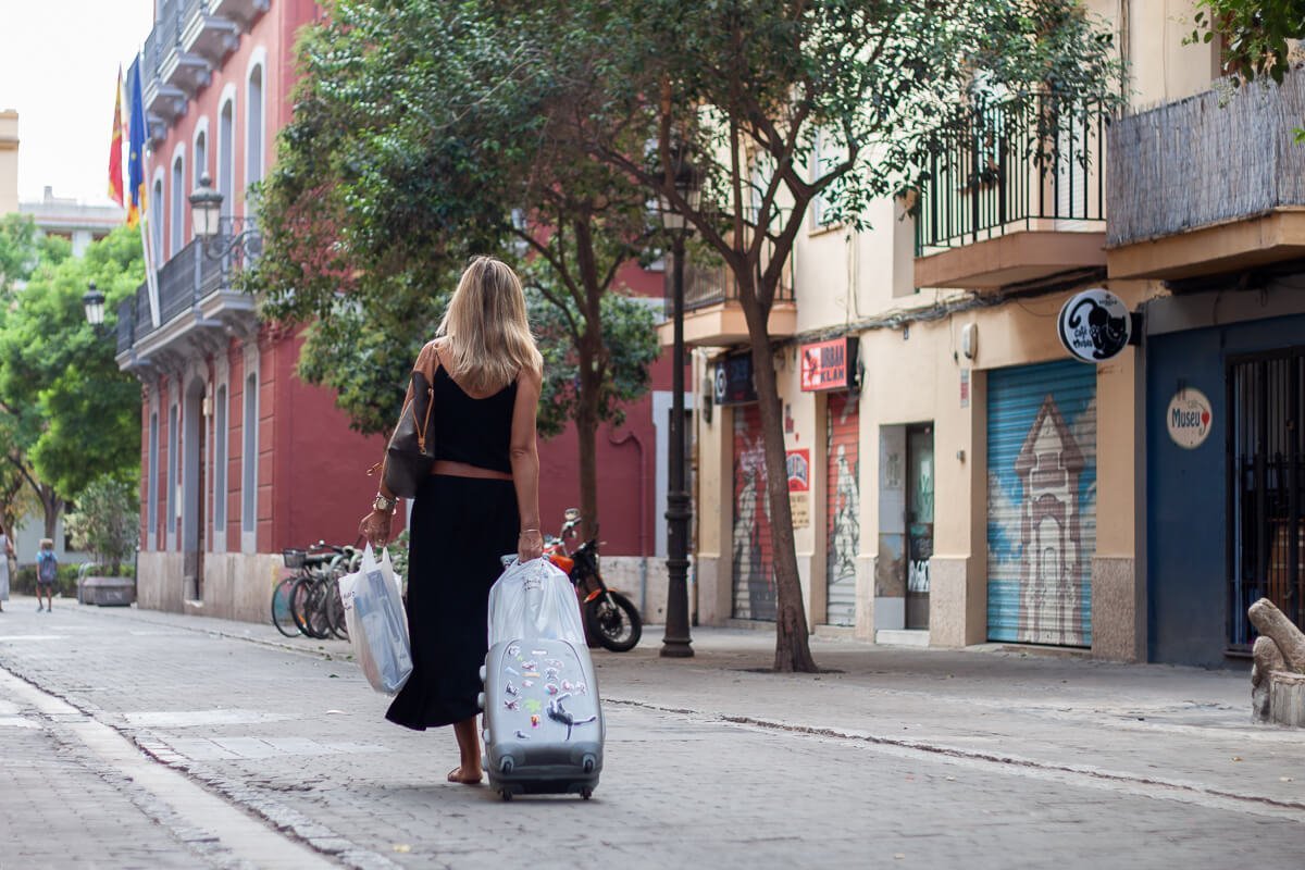 Valencia woman rolling small suitcase and plastic bags over street in El Carmen neighbourhood.