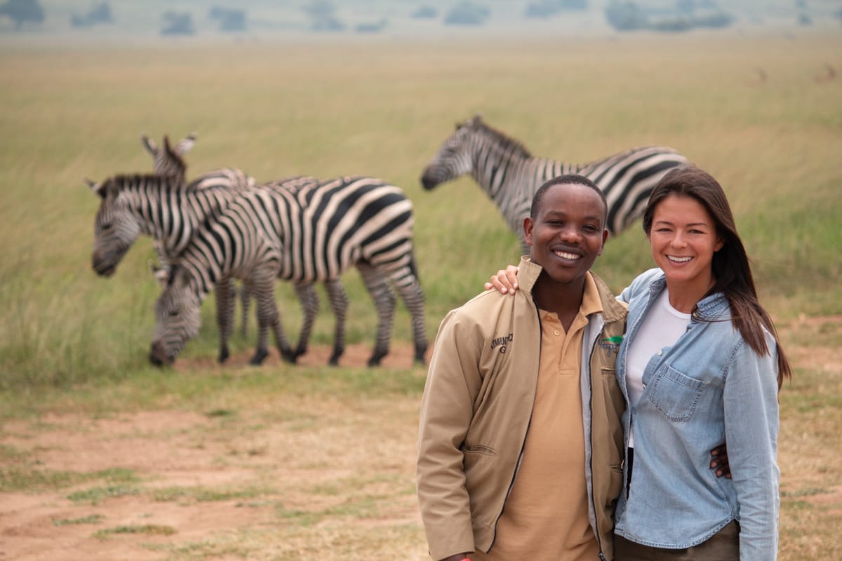 Our guide Samuel and Kim post in front of zebras in Akagera Park